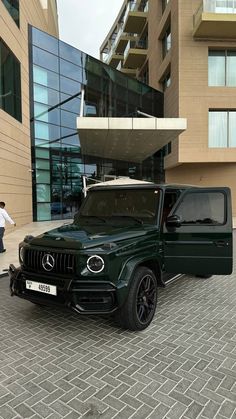 a green mercedes benz truck parked in front of a building with people walking around it