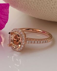 a pink flower sitting next to a gold ring on top of a table with white and pink flowers in the background