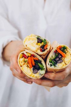 a person holding three burritos filled with veggies