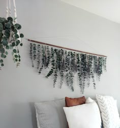 a white bed topped with lots of pillows next to a plant wall hanging on the wall