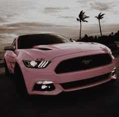 a pink mustang car parked in front of palm trees on the beach at sunset or dawn