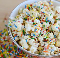 a bowl filled with sprinkles and popcorn on top of a wooden table