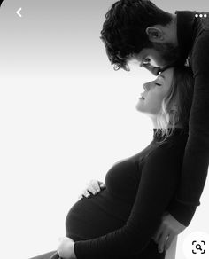 a pregnant woman leaning on the back of a man's head while he kisses her belly