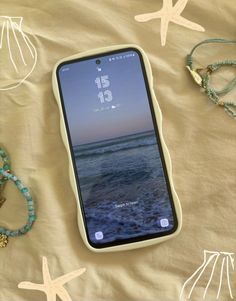 a cell phone laying on top of a bed next to bracelets and starfish