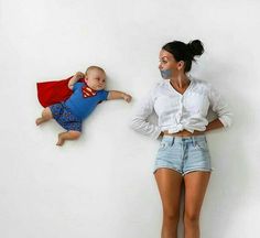 a woman standing next to a baby wearing a superman costume