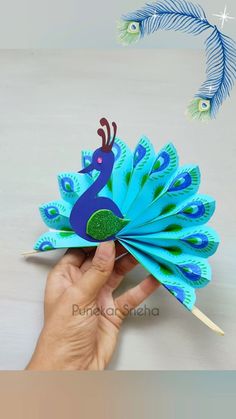 a hand holding a paper peacock on top of a table