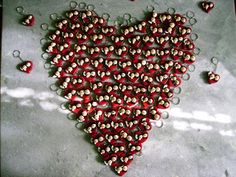 a heart made out of small beads on top of a cement surface with water droplets around it