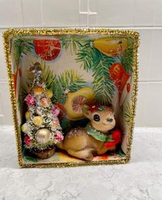 a deer figurine sitting next to a christmas tree in a box on a counter