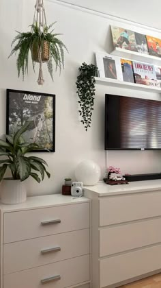 a flat screen tv sitting on top of a white dresser next to a potted plant