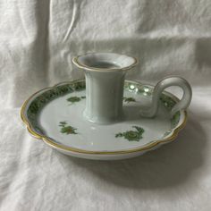 a cup and saucer sitting on top of a white cloth covered tablecloth with gold trimmings