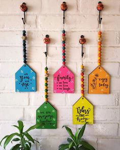 colorful wooden tags hanging on the wall with beaded necklaces and plants in front of them