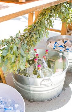 two metal buckets filled with bottles and ice on top of a cement floor next to a wooden table