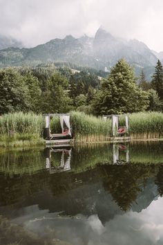 there are two chairs that are sitting on the shore of a lake in front of some mountains