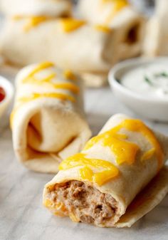 two burritos with cheese and sauce on the wrapper next to dipping sauce