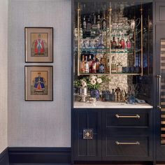 a bar with liquor bottles and glasses on the shelves in front of it, next to two framed pictures