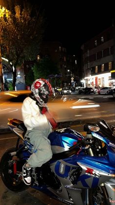 a man riding on the back of a blue motorcycle down a street at night time