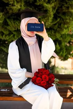 a woman sitting on a bench holding a bouquet of red roses in front of her face