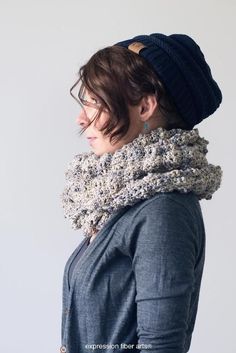 a woman wearing a knitted scarf and beanie looks off to the side while standing against a white background