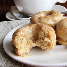 three glazed donuts on a white plate next to a cup