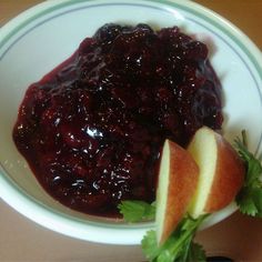 a bowl filled with cranberry sauce next to an apple on top of a table