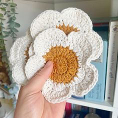 a crocheted flower is held up in front of a bookshelf