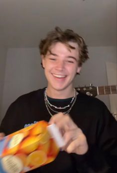 a young man is smiling and holding a bag of oranges in front of him