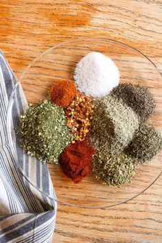 various spices are on a glass plate next to a blue and white dish towel that is sitting on a wooden table