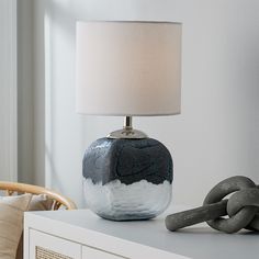 a lamp sitting on top of a table next to a white dresser with a chain