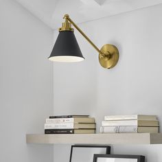 a black and gold lamp on a white wall next to a shelf filled with books