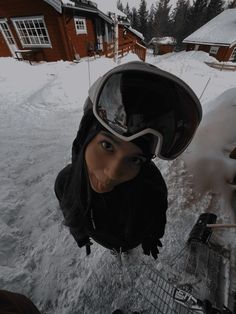 a woman wearing a helmet and goggles standing in the snow next to a house