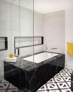 a black and white bathroom with a bathtub next to a yellow towel hanging on the wall