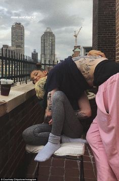 two people are sitting on a ledge with their backs to each other and one person is bending over