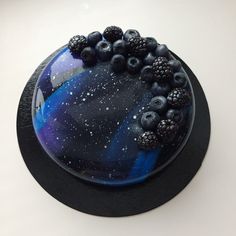 a blue and black cake with berries on it sitting on top of a white table