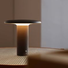 an illuminated table lamp sitting on top of a wooden table next to a white wall