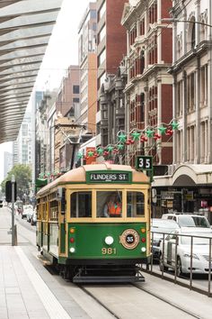 a green trolley car traveling down a street next to tall buildings and parked cars on the side of the road