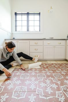 a woman is laying on the floor in her kitchen and painting it with white paint