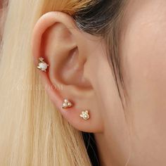 a woman with blonde hair wearing three different ear piercings on her left side, and two small white stones in the middle