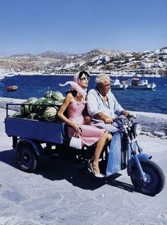 a man and woman riding on the back of a motorcycle with watermelons in the back