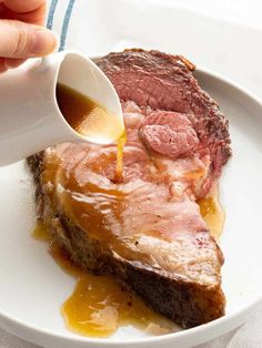 a person pouring sauce on top of a piece of meat