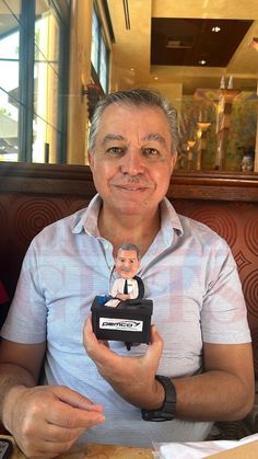 a man sitting at a table with a doll in front of him holding a small figurine