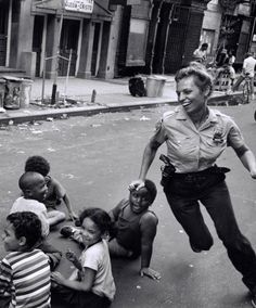 a woman police officer is dancing in the street with children on the ground and people sitting around her