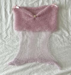 a piece of pink knitted material sitting on top of a white bed sheet,