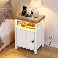 a night stand with an alarm clock on it next to a bed