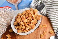 a white bowl filled with cheetos sitting on top of a wooden cutting board