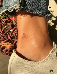 a small cherry tattoo on the side of a woman's ankle, with red cherries