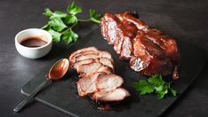 some meat is on a black plate with sauces and parsley next to it