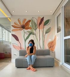 a woman sitting on a couch in front of a wall with flowers painted on it