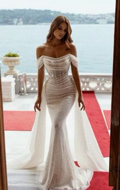 a woman standing in front of a doorway wearing a white dress with an off the shoulder design