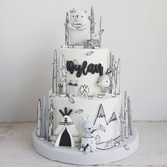 a three tiered cake decorated with black and white doodles, animals and trees