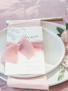 a table setting with pink flowers and napkins on the plate, along with a menu